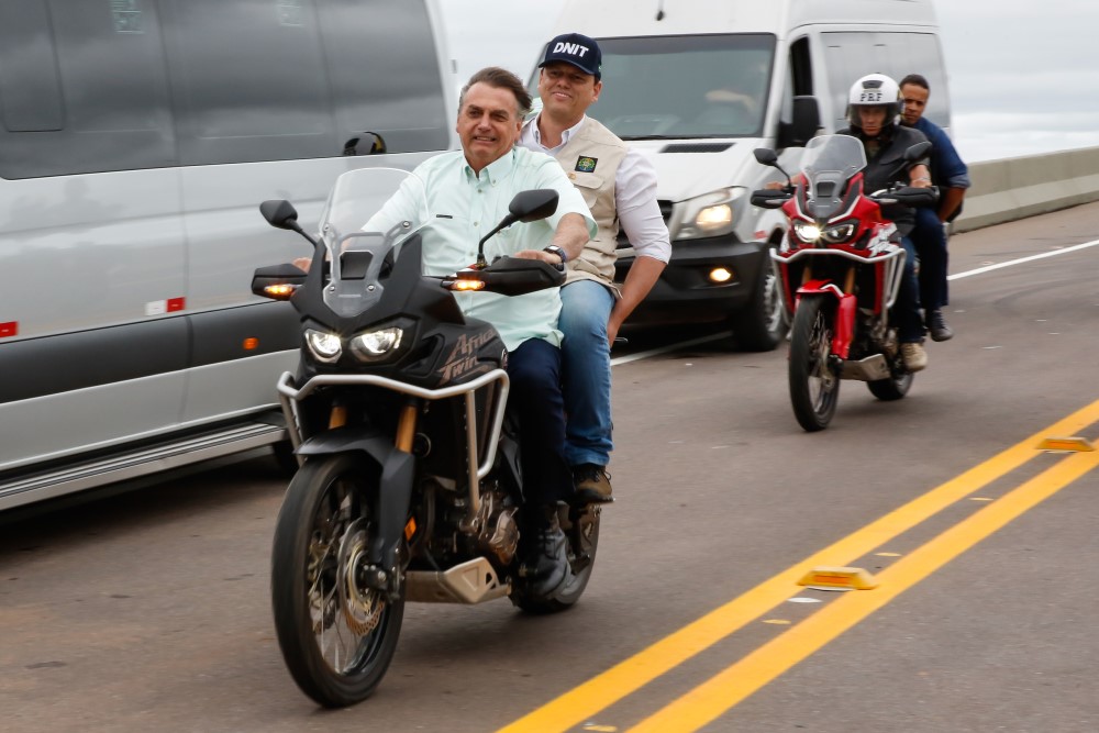 Bolsonaro passeia de moto em uma via, com carros ao lado e o ministro Tarcísio na garupa
