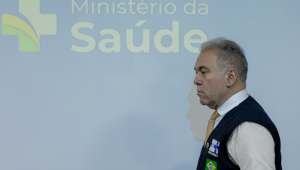 O ministro Marcelo Queiroga de perfil, vestindo colete, passando em frente a uma parede onde está escrito o nome Ministério da Saúde