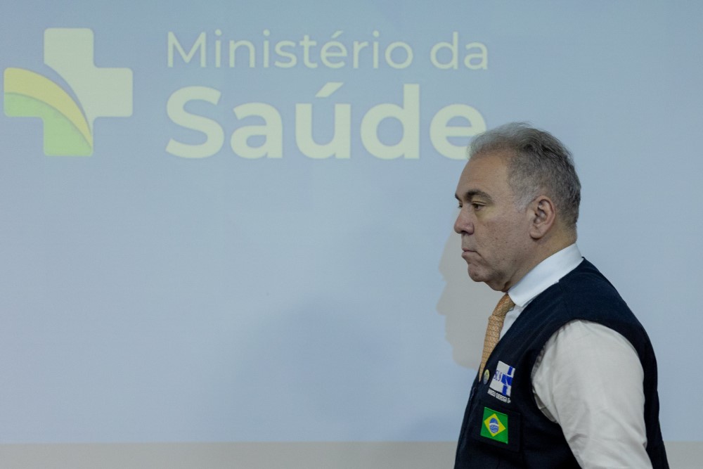 O ministro Marcelo Queiroga de perfil, vestindo colete, passando em frente a uma parede onde está escrito o nome Ministério da Saúde