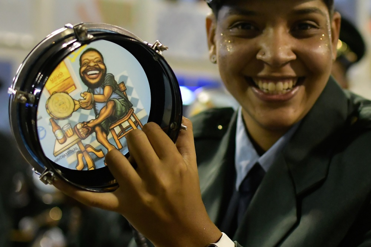 Integrante da bateria da Vila Isabel sorri ao mostrar tamborim com a imagem de Martinho da Vila, homenageado no desfile da escola em 2022