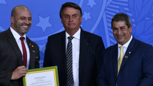 presidente da república, Jair Bolsonaro, acompanhado do deputado Daniel Silveira, segurando um quadro com quadro com decreto de Bolsonaro, e o deputado Coronel Tadeu