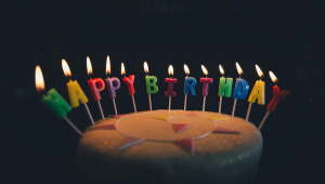 Bolo de aniversário com velas no formato das letras que formam as palavras Happy Birthday acesas