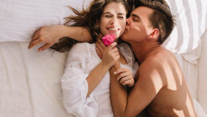 Retrato aéreo de jovem sonolento bronzeado com penteado da moda beijando sua linda namorada, deitada na cama com os olhos fechados