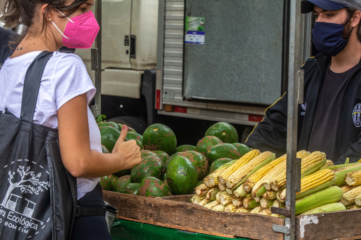 Cliente de máscara observa frutas e legumes em barraca de fruta