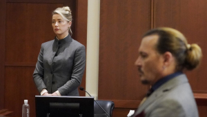 Amber Heard, de pé, em um tribunal do júri; à frente dela, Johnny Depp, sentado