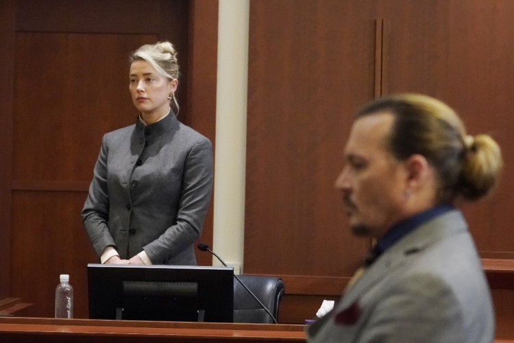 Amber Heard, de pé, em um tribunal do júri; à frente dela, Johnny Depp, sentado