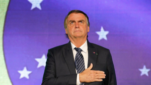 De terno e gravata, Jair Bolsonaro coloca a mão no peito durante o hino