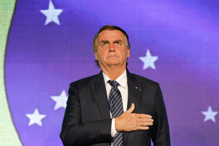 De terno e gravata, Jair Bolsonaro coloca a mão no peito durante o hino