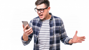 Jovem de óculos segura o celular enquanto faz cara de bravo