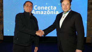 Jair Bolsonaro aperta a mão de Elon Musk em frente a um painel do Conecta Amazônia