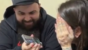 Homem segura celular enquanto mulher, com a mão na frente do rosto, fala em uma ligação