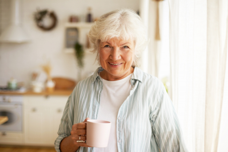 Mulher idosa sênior com aparência amigável e positiva, com cabelos grisalhos e rugas, passando o dia em casa, bebendo chá