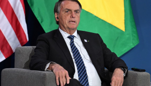 Sentado, Jair Bolsonaro fala em frente à bandeiras do Brasil e dos Estados Unidos