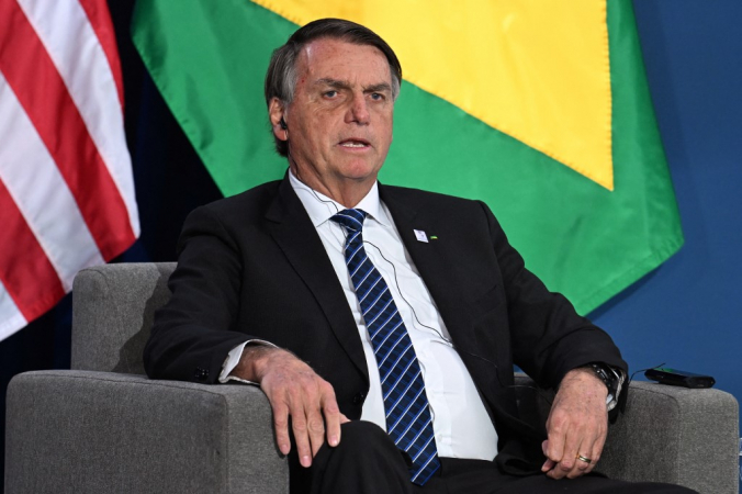 Sentado, Jair Bolsonaro fala em frente à bandeiras do Brasil e dos Estados Unidos