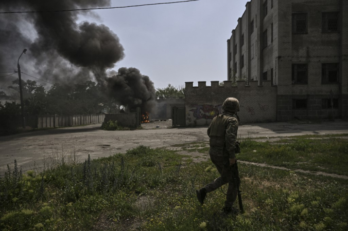Militar ucraniano caminha na frente de um veículo em chamas durante um duelo de artilharia entre tropas ucranianas e russas na cidade de Lysychansk, região leste ucraniana de Donbass