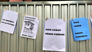 Quatro cartazes colados em um portão de alumínios, os quais dizem sem memória não há futuro, a diversidade de Pinheiros mora aqui, mais casas, menos prédios, mais verde, menos concreto