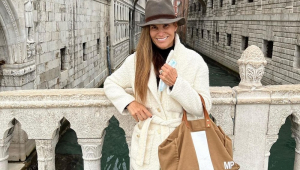 Mariana Papa, uma mulher na faixa dos 40 anos, posa agasalhada e usando bolsa e chapéu em uma ponte em Veneza