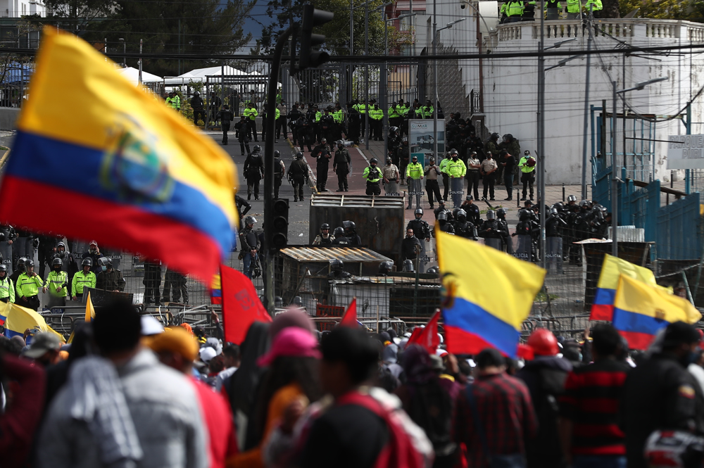 Manifestantes com bandeiras do Equador são observados por policiais