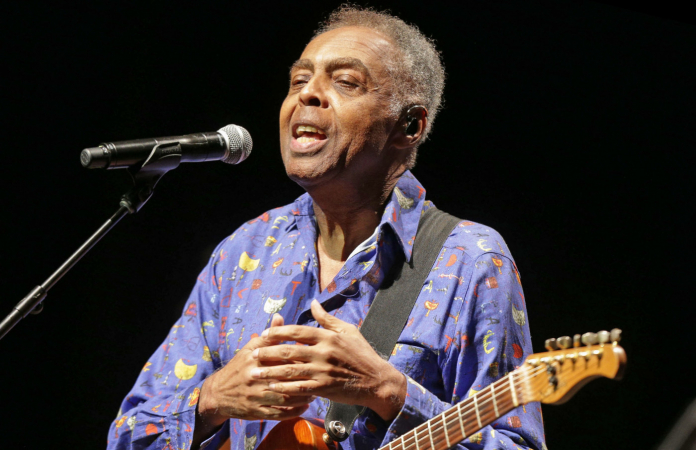 De camisa azul estampada e guitarra a tiracolo, Gilberto Gil entreçlaça as mãos durante show