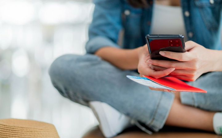 Mão do viajante feminino segurando o passaporte usando o smartphone para verificar on-line para embarque no aeroporto