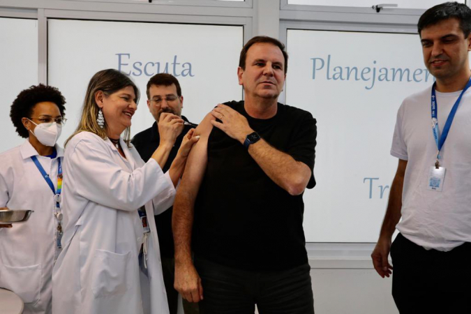 Prefeito Eduardo Paes usa roupa preta, relógio preto, enquanto toma vacina