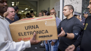 Funcionários do TSE carregam caixa na qual se lê "urna eletrônica"