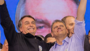 Marcos Pontes, segurando uma bandeira, Bolsonaro e Tarcísio, os três em pé, abraçados e apontando para o alto