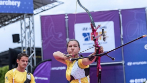 Atleta brasileira atira com arco; companheiro de dupla observa ao fundo
