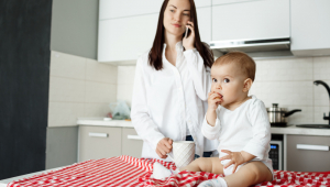Mãe tomando café e falando ao telefone enquanto o bebê come na mesa da cozinha