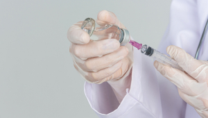 Jovem médico está segurando a seringa hipodérmica com luvas de borracha do frasco de remédio