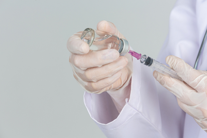 Jovem médico está segurando a seringa hipodérmica com luvas de borracha do frasco de remédio