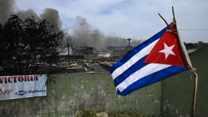 Uma bandeira cubana tremula perto de uma área destruída do depósito de combustível que foi envolvido em chamas por cinco dias depois que um raio atingiu um de seus tanques