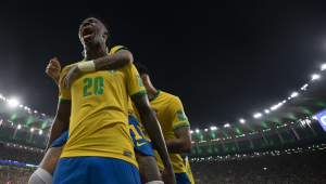 Vinicius Junior solta um grito após marcar um gol pela seleção brasileira no Maracanã, e jogadores chegam atrás dele para comemorar