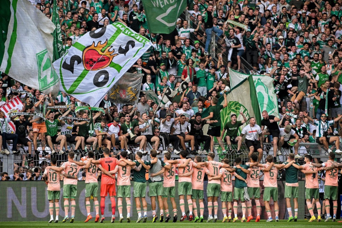 De costas para imagens, abraçados e perfilados, Werder Bremen comemora vitória em Dortmund com a torcida
