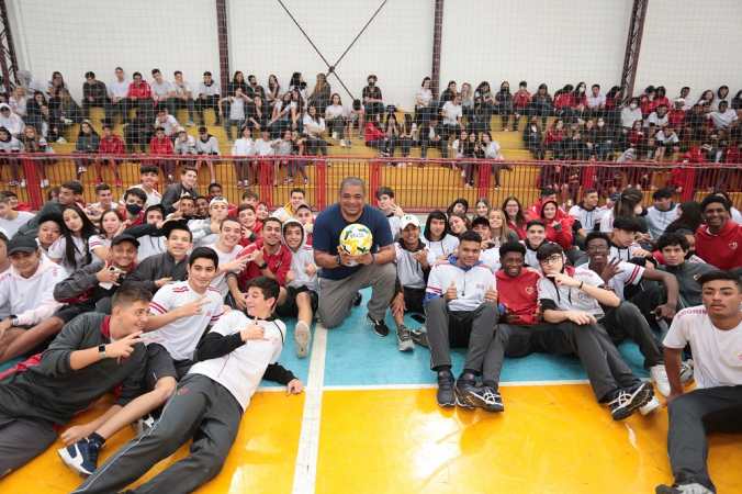 Vampeta no centro da quadra, segurando bola, cercado por alunos do Colégio Amorim