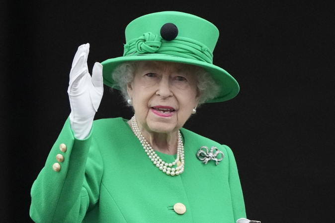 Rainha Elizabeth II acena para o público de dentro do Palácio de Buckingham