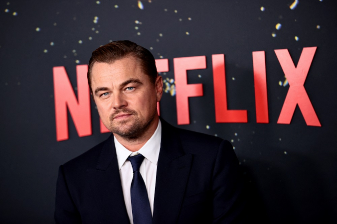 Leonardo DiCaprio em frente a um painel preto com o logo da Netflix em vermelho