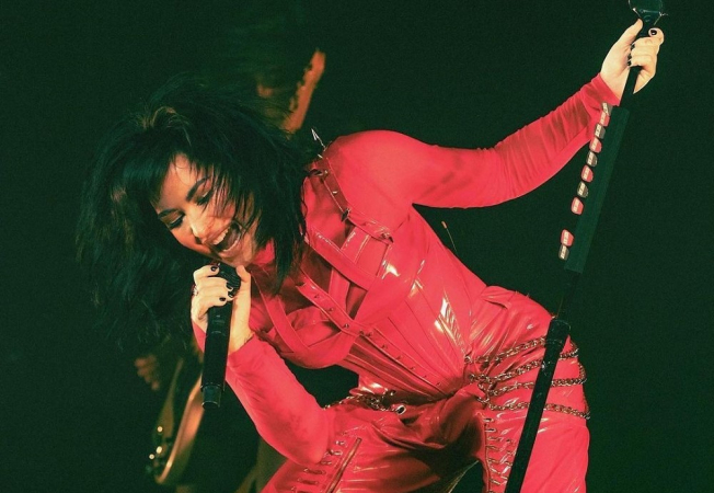 De roupa latex vermelha, Demi Lovato se curva e fecha os olhos para cantar