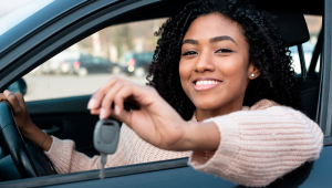 Mulher jovem negra mostra a chave do carro e sorri dentro do automóvel