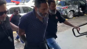 Homem preso e algemado é levado por agentes da polícia