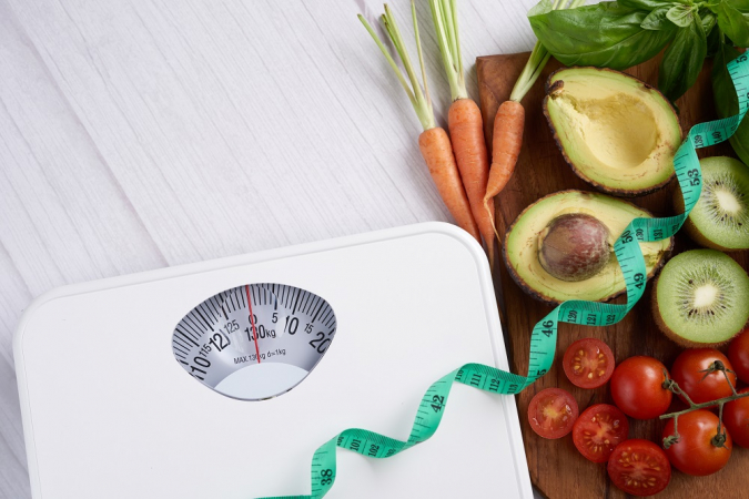 Foto conceitual sobre perda de peso, com balança, fita métrica, frutas e legumes