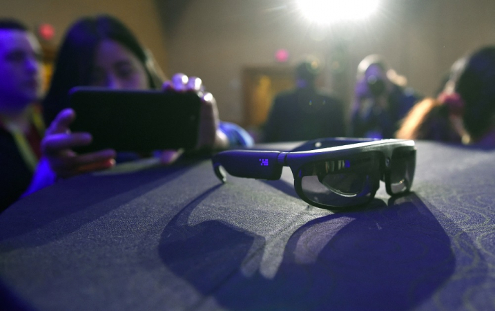 Jovem mulher tira foto de smartglasses expostos em feira tecnológica