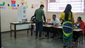 Um homem de verde e uma mulher com a bandeira do Brasil enrolada na cintura falam com mesários antes de votar
