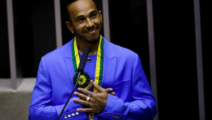 Vestido de terno azul, Lewis Hamilton reage após receber o título de cidadão honorário do Brasil na Câmara dos Deputados