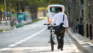 Homem vestido com trajes sociais caminha carregando a bicicleta em corredor de ônibus