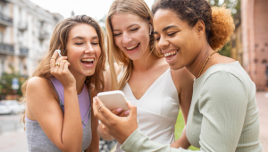 Mulheres assistem a vídeo no celular e riem em espaço público