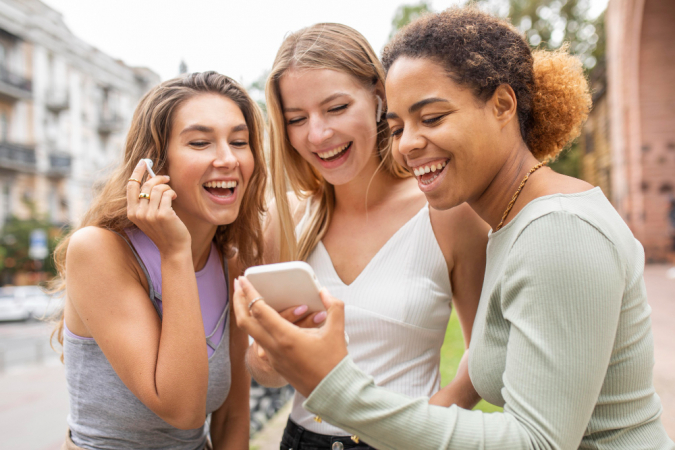 Mulheres assistem a vídeo no celular e riem em espaço público