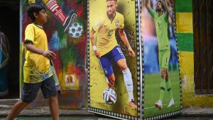 Um menino passa por uma parede decorada com cartazes mostrando as imagens de Neymar e Alisson pintadas em paredes de Calcutá