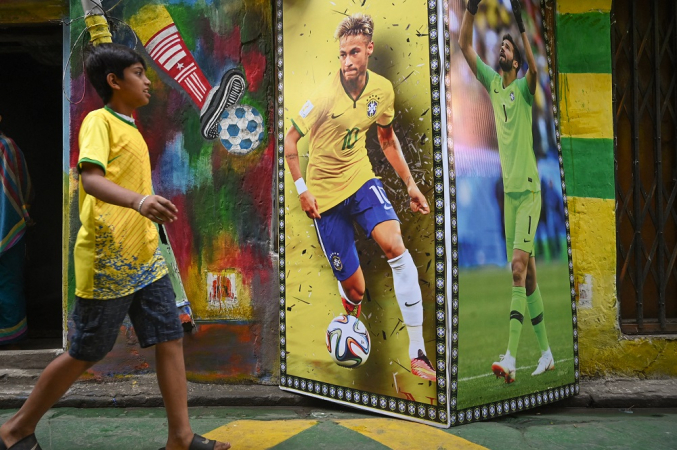 Um menino passa por uma parede decorada com cartazes mostrando as imagens de Neymar e Alisson pintadas em paredes de Calcutá