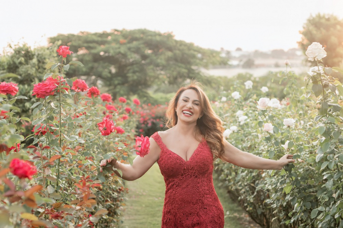 Mulher branca de vestido vermelho caminha sorridente em jardim